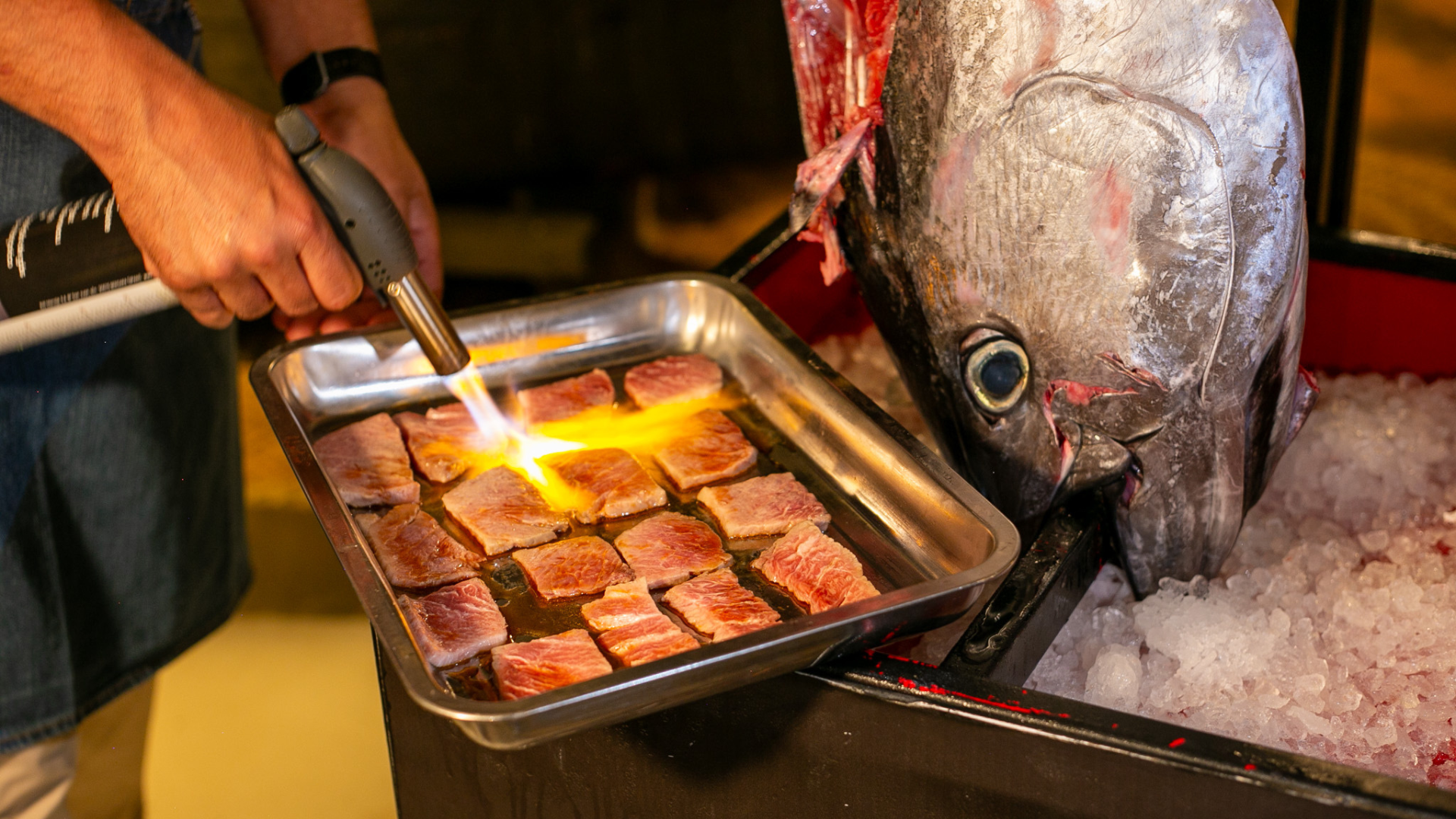 Chef flambeando lingotes de atún oro, mostrando un espectáculo culinario tras el ronqueo de atún, para un evento exclusivo.