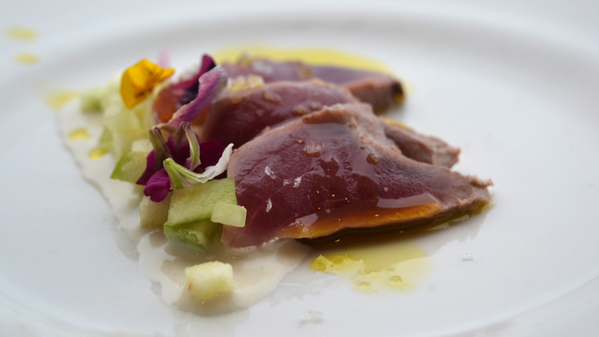Lingote de Atún Oro Tataki, presentado elegantemente con ajoblanco de pepino y manzana, listo para ser disfrutado tras un show de ronqueo de atún.