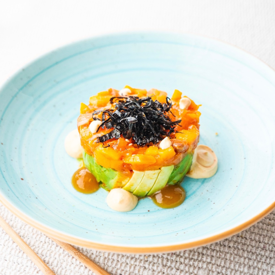 Tataki de salmón fresco acompañado de aguacate en rodajas, servido como plato gourmet.