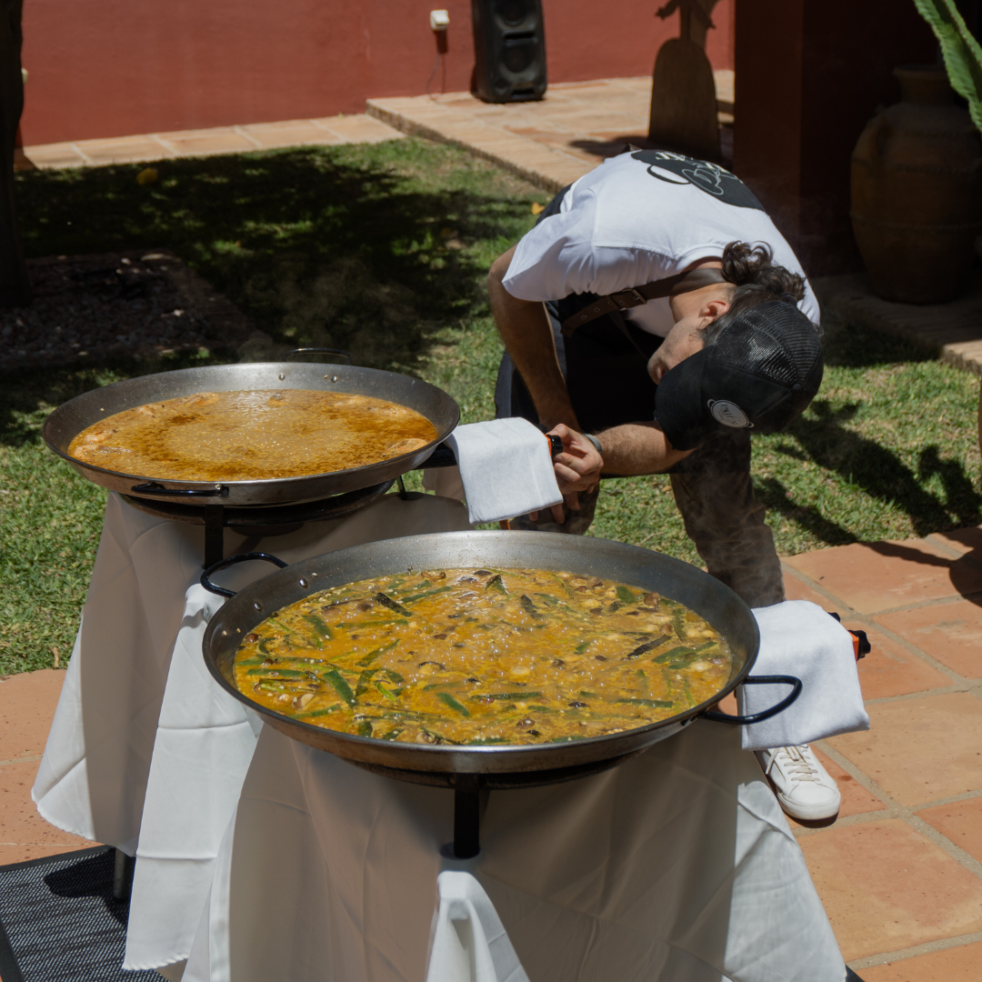Chef arrocero cocinando dos paellas al mismo tiempo durante un evento privado, deleitando a los invitados con sabores auténticos.
