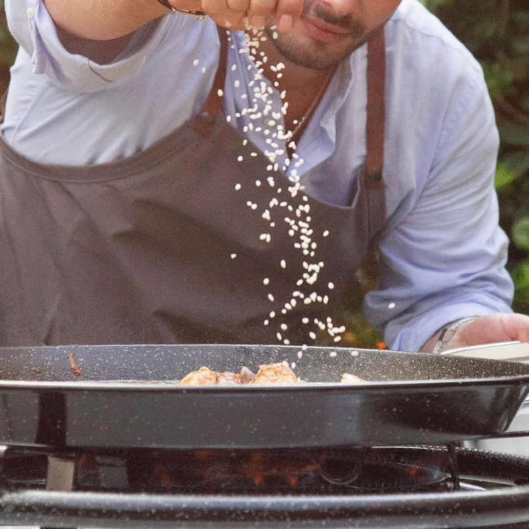 Chef arrocero echando el arroz en la paella durante un show cooking de paella para un evento privado.